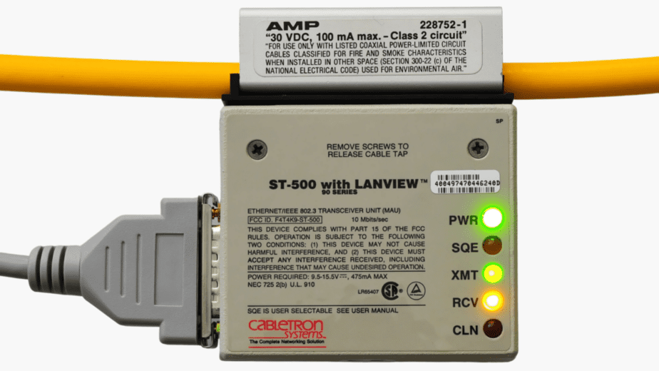 Conector transceiver MAU ST-500 com conector vampiro utilizado em cabos Thicknet 10BASE5, exibindo indicadores LED de atividade e conexão em redes Ethernet antigas.