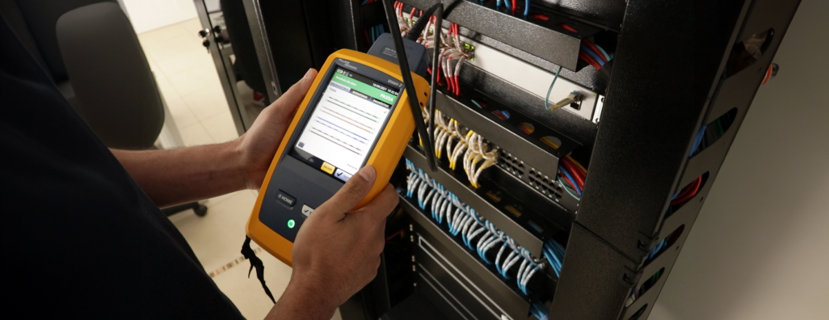 Profissional de TI usando um aparelho certificador para configurar uma rede em um rack de servidor bem organizado.