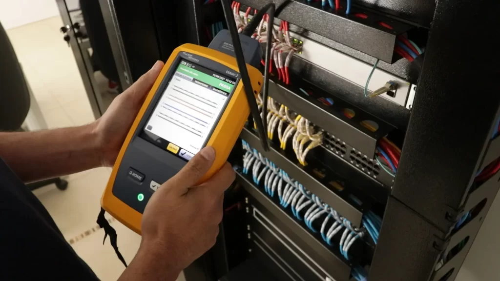 Técnico realizando a certificação do cabeamento de rede, em frente a um rack de cabeamento estruturado.