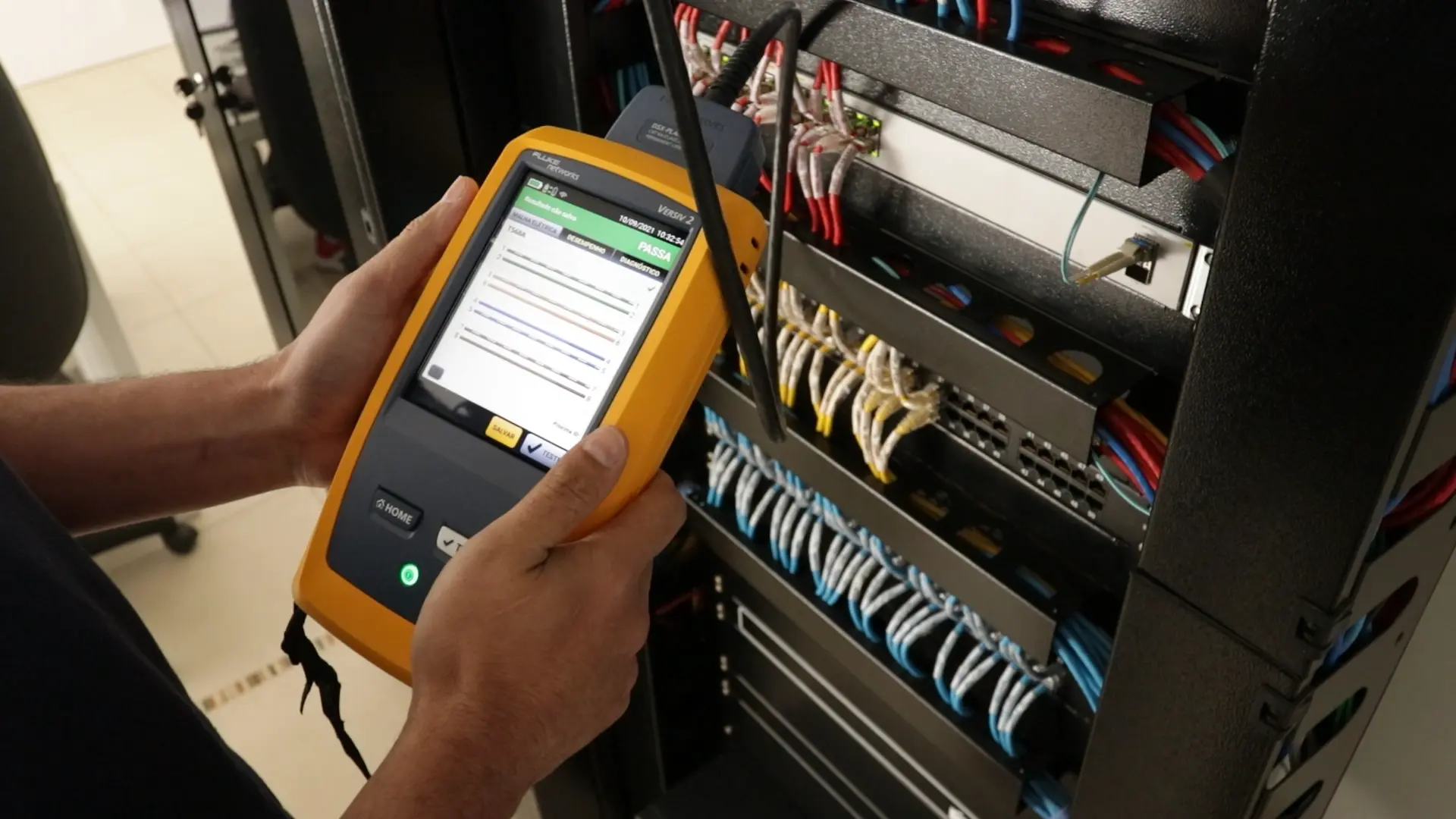 Técnico realizando a certificação do cabeamento de rede, em frente a um rack de cabeamento estruturado.