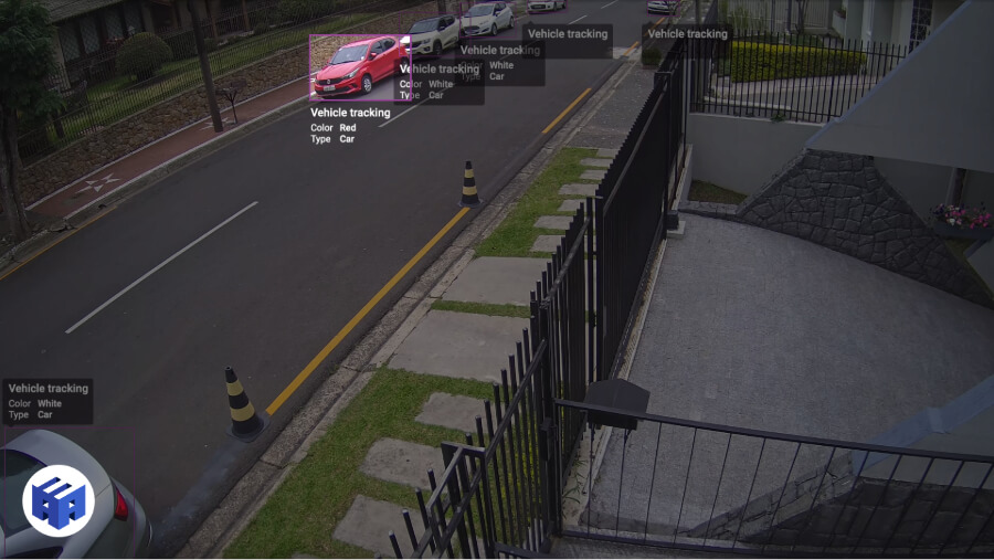 Screenshot de uma câmera 4K com IA (modelo Hanwha Vision PNO-A9081R) exibindo a funcionalidade de identificação de características de veículos. A imagem mostra uma rua monitorada, onde a inteligência artificial detecta e classifica carros com base em cor e tipo, destacando um veículo vermelho com uma caixa de rastreamento. Essa tecnologia avançada de videomonitoramento permite análise automatizada para segurança perimetral, controle de tráfego e identificação em tempo real.