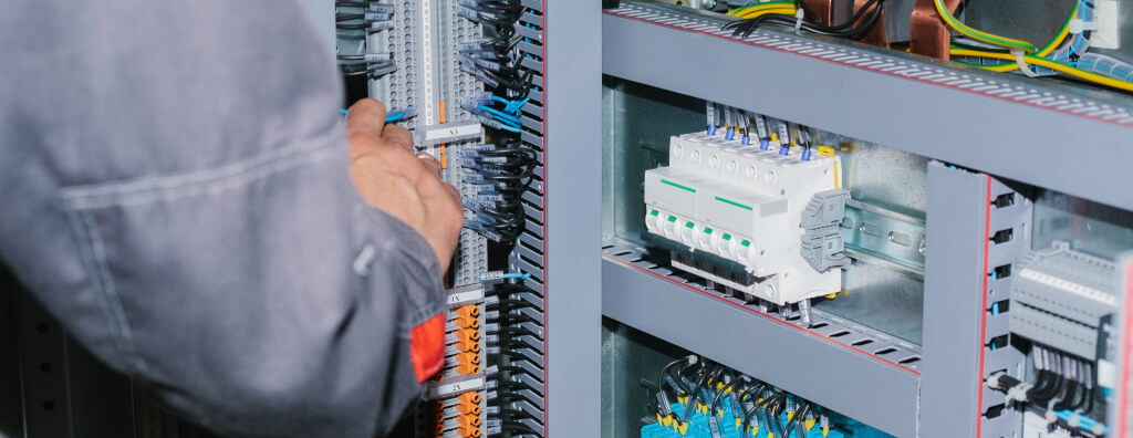 Técnico realizando manutenção em quadro elétrico com barramentos, cabos e disjuntores em instalação elétrica de baixa tensão