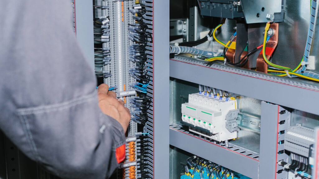 Empresa de Projetos Elétricos: Técnico realizando manutenção em quadro elétrico com barramentos, cabos e disjuntores em instalação elétrica de baixa tensão